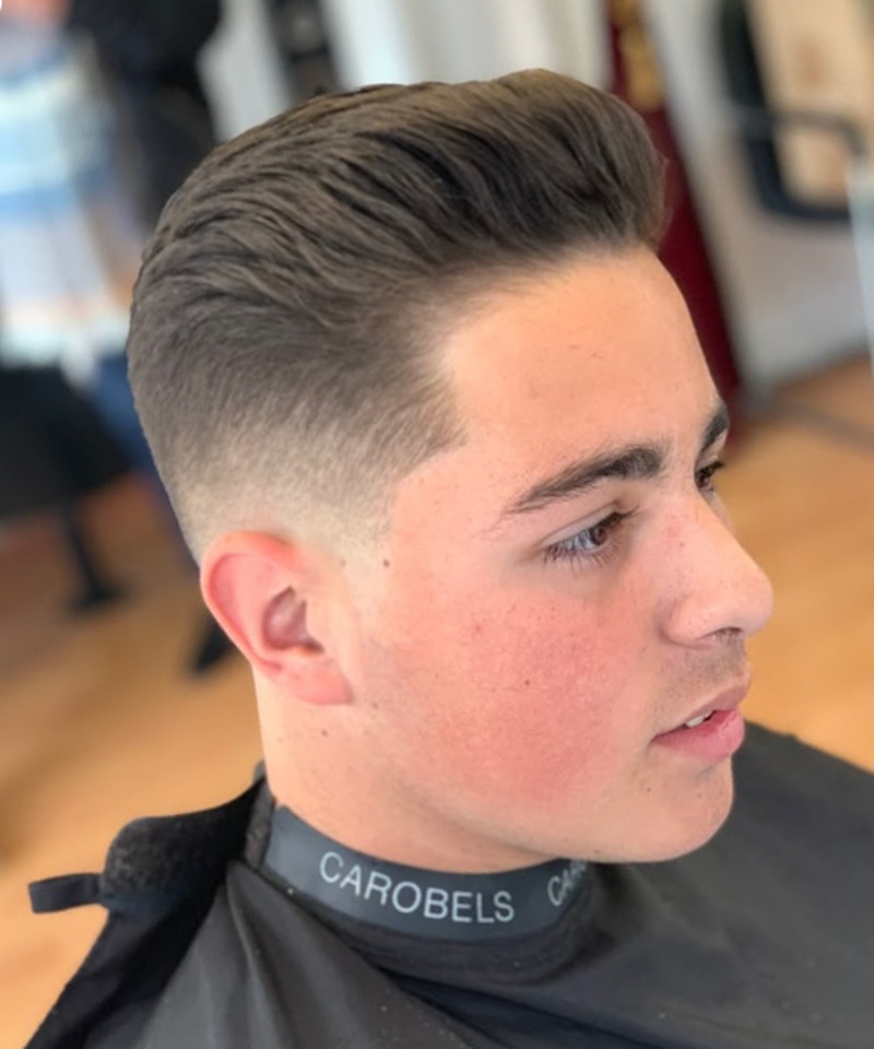 A low fade haircut with textured, swept-back top hair and a clean, gradual transition from longer hair on top to closely shaved sides.