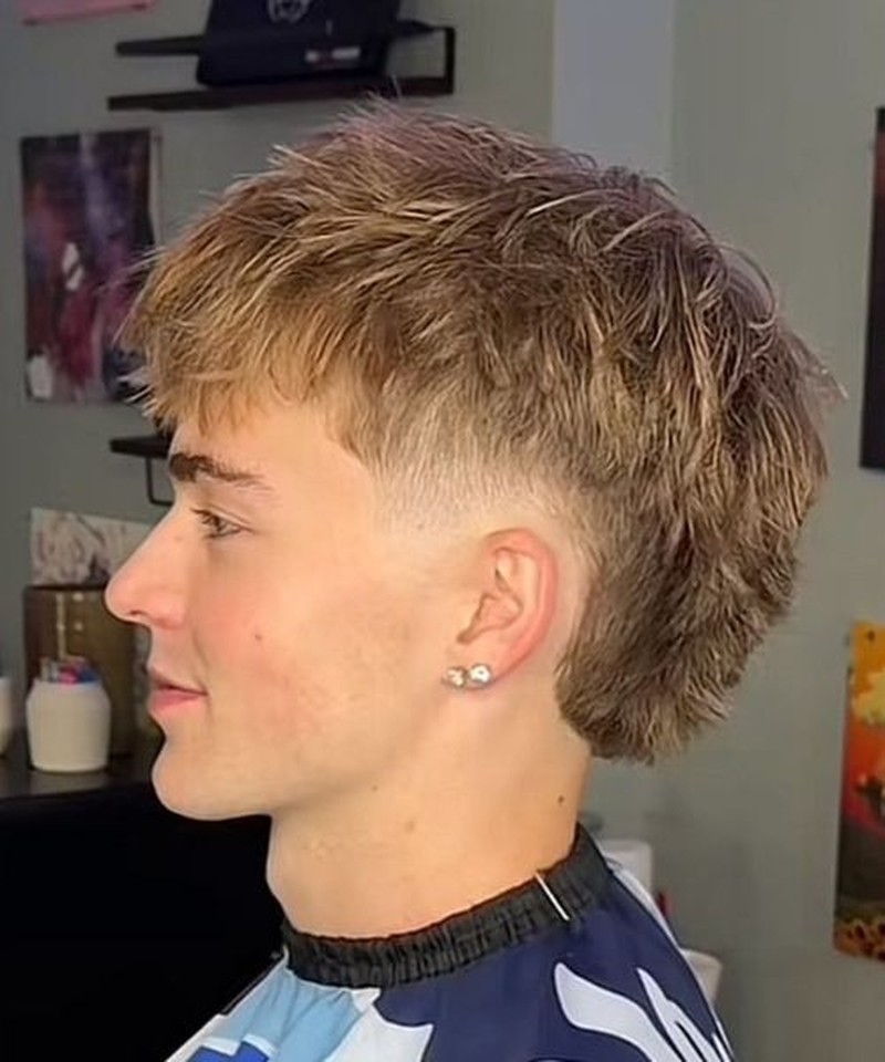 A man with a short textured layered mullet featuring a low fade transition with tousled medium-length top hair and closely shaved sides