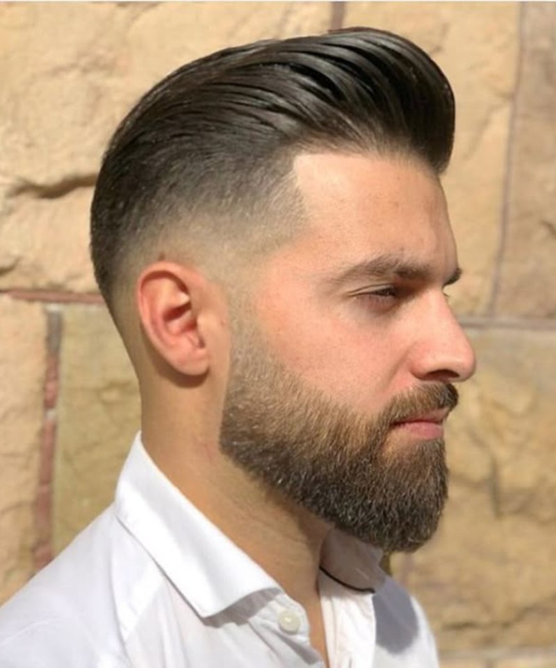 A sharp low fade with closely shaved sides, a textured, swept-back top, and a polished, modern finish.