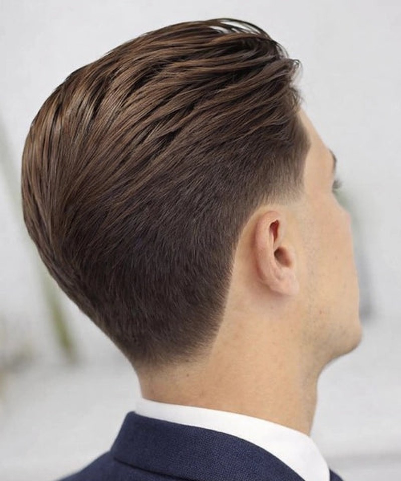 A short, neat fade haircut with longer, styled brown hair on top, combed back smoothly, and a clean, gradual taper down the sides and back.