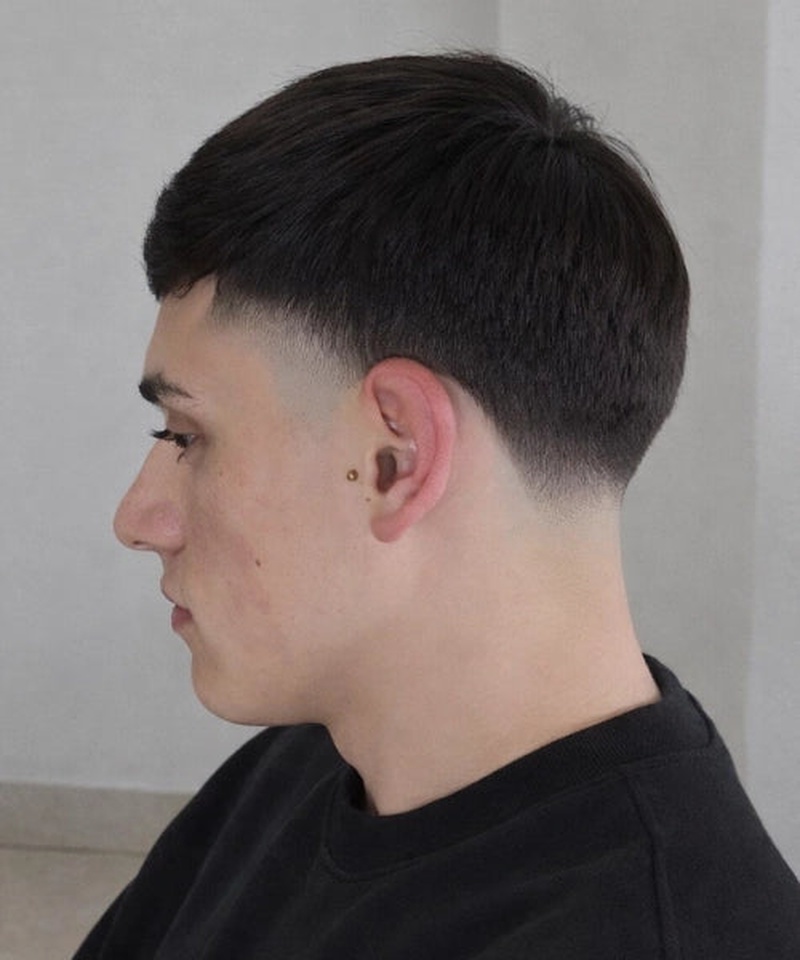 A short, neatly styled haircut with a clean low fade transitioning from closely shaved sides to longer, textured top hair.