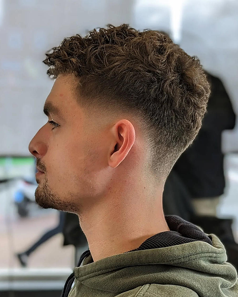 Curly textured top with a bald drop fade, blending volume on top to a clean, sharp fade down the sides.