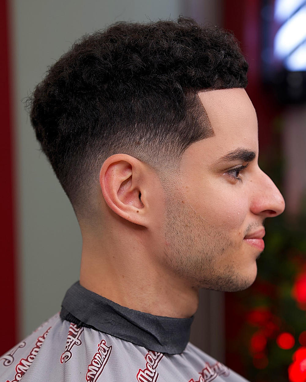 Curly top with textured volume, low fade, sharp hard part, clean skin fade transition.