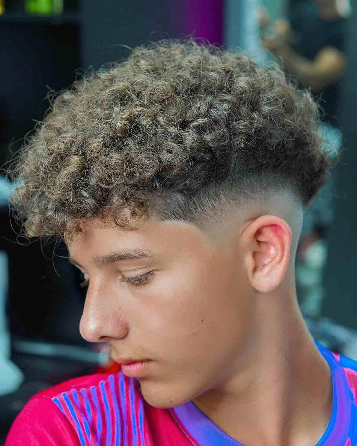 Drop fade with V-cut nape, curly textured top, sharp fade transition, visible V-shape at back.