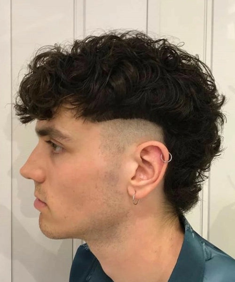 Men's buzz top mullet haircut with curly texture and fade sides.