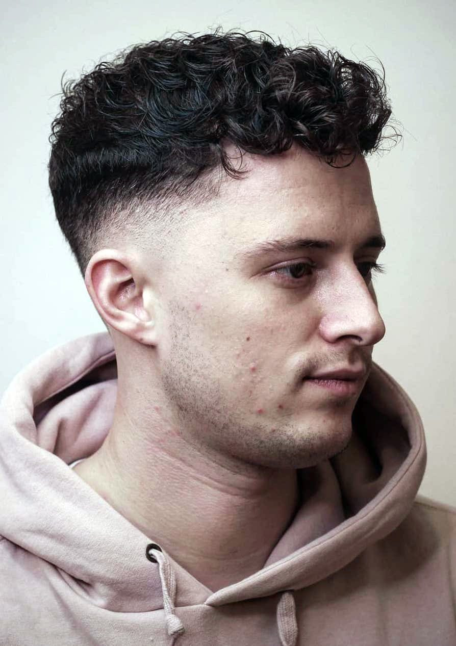 Messy, textured top with defined curls; sharp drop fade tapers from mid-lengths to clean skin.