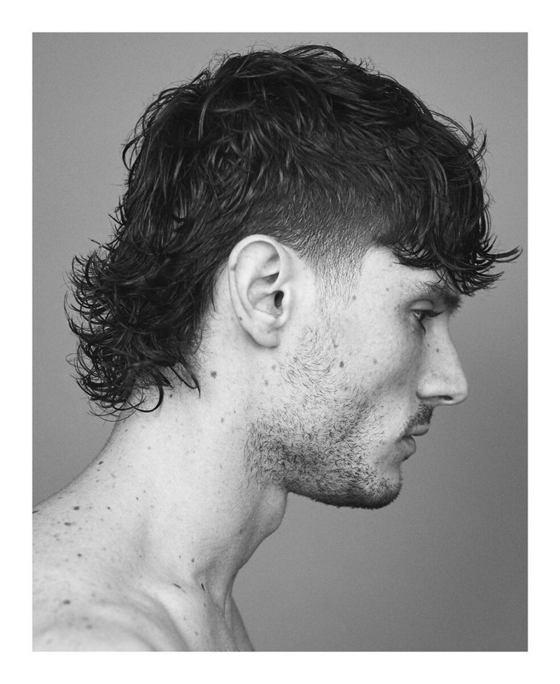 Side view of a man with curly, dark hair styled in a fluffy mullet variation featuring a fade cut.
