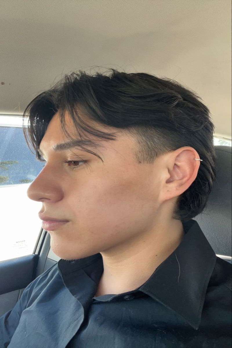 Side view of a man with thick, dark brown hair styled in a fluffy mullet variation, featuring a textured top and tapered sides.