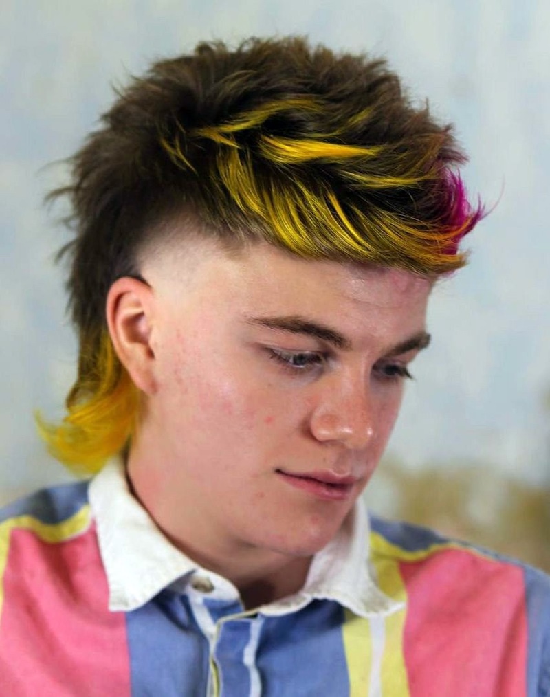 Side view of a man with thick, fluffy hair featuring a mullet variation, with brown base color, yellow and pink highlights, and a textured, voluminous cut.
