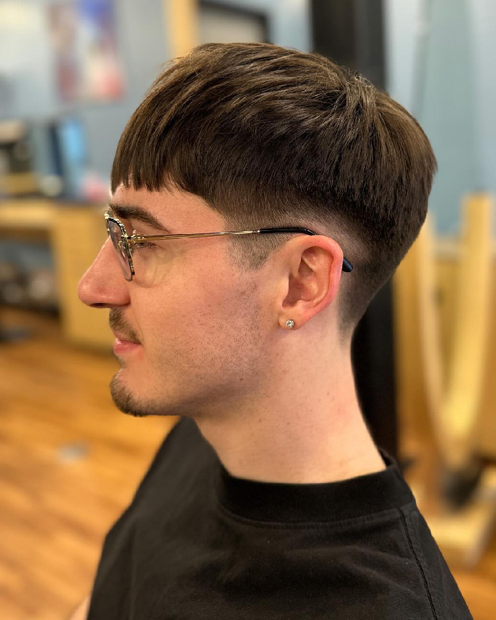 Textured, medium-length top with straight-cut bangs, low fade, and a small ear piercing.