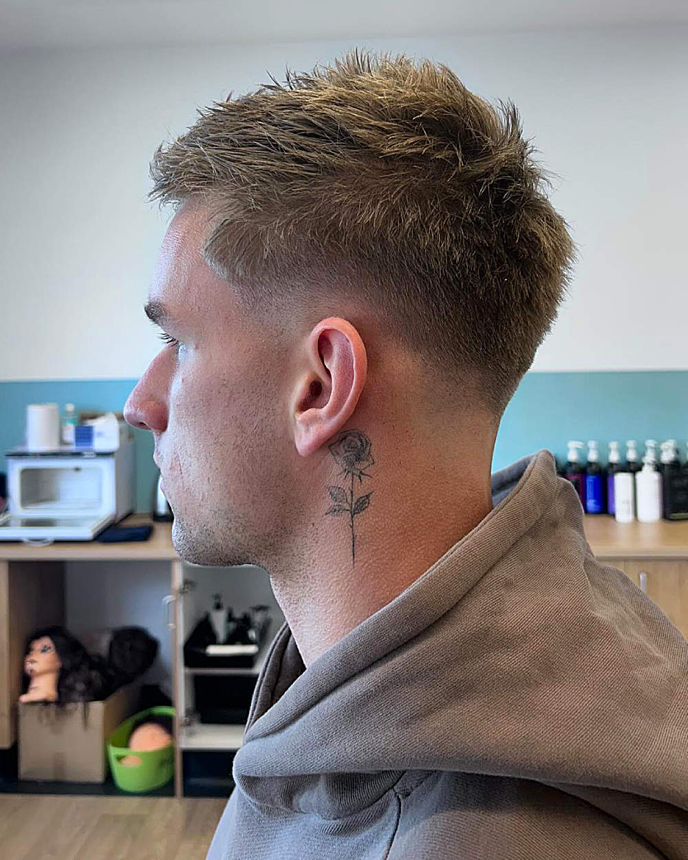 Textured, spiky men’s haircut with a high fade and a rose tattoo behind the ear.