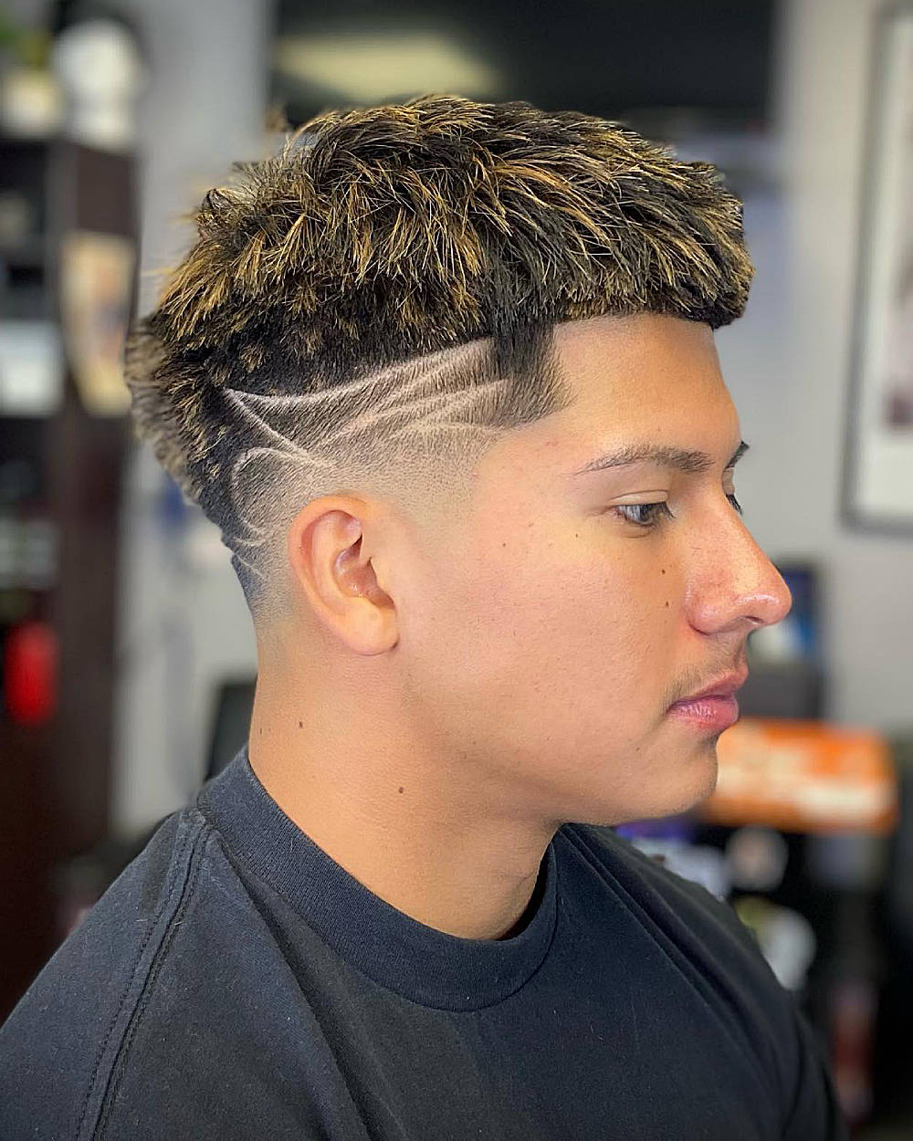 Textured, spiky top with blonde highlights; mid fade, sharp geometric side design.