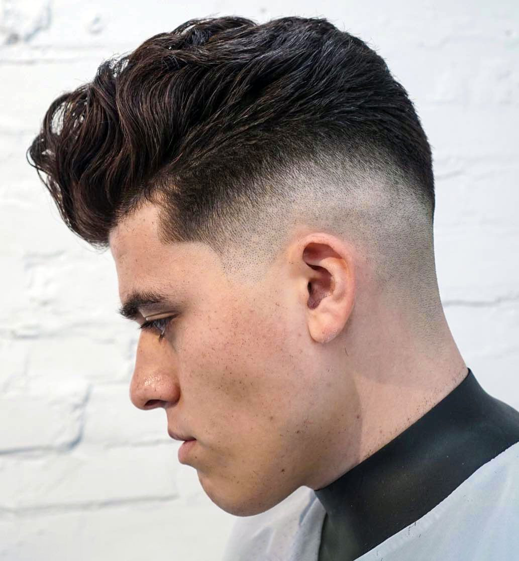 Textured, swept-back men’s haircut with high skin fade, defined waves, and clean, sharp lines.