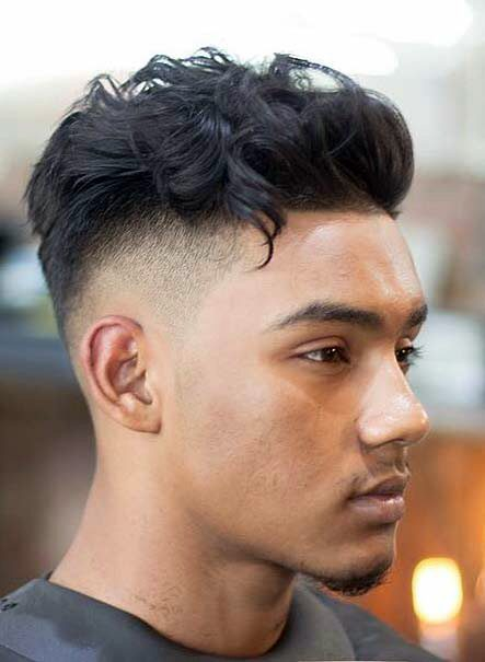 Wavy, textured top with a mid drop fade; hair styled upward, gradual fade from longer top to shorter sides.