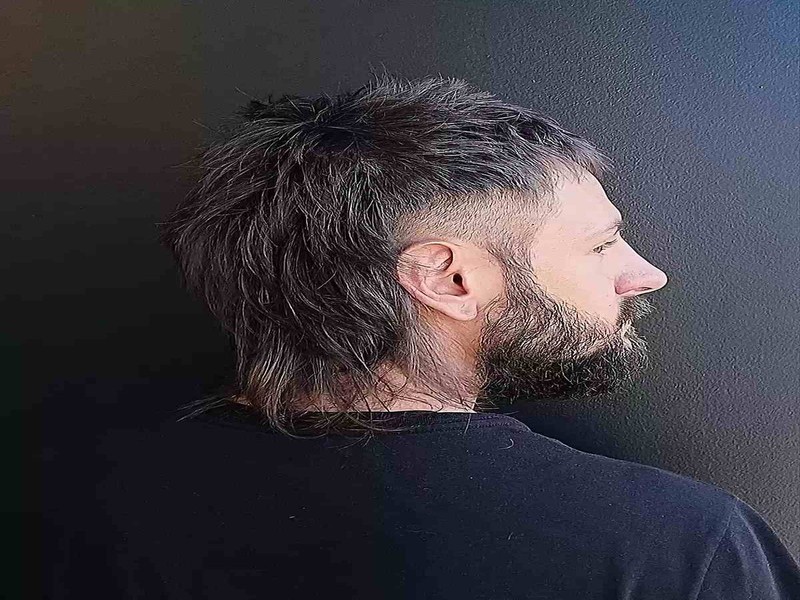 Man with a choppy mullet haircut showing textured medium-length hair, low fade, and messy, tousled style.