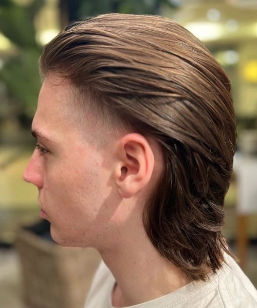 Man with a surfer mullet haircut showing medium-length, textured slick-back, low fade, and tapered sides.