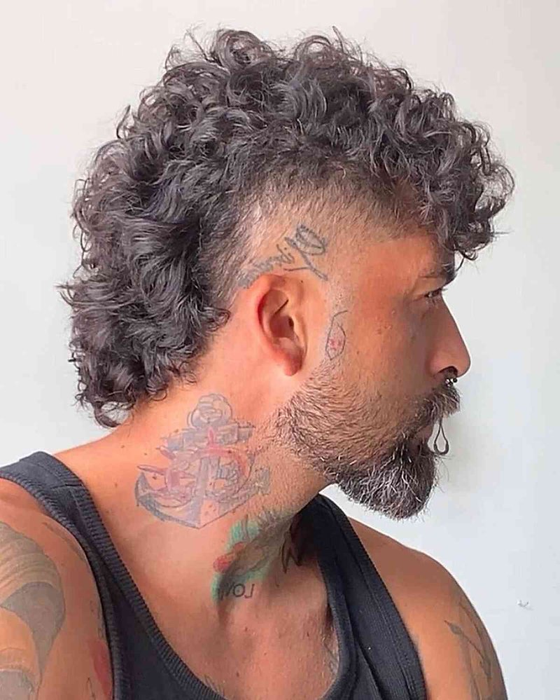 Man with a coiled mullet haircut showing curly gray hair, high skin fade, textured medium length.