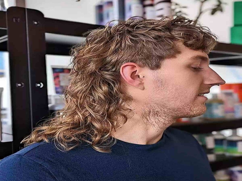 Man with a kinky mullet haircut showing long curly hair, textured top, and low fade.