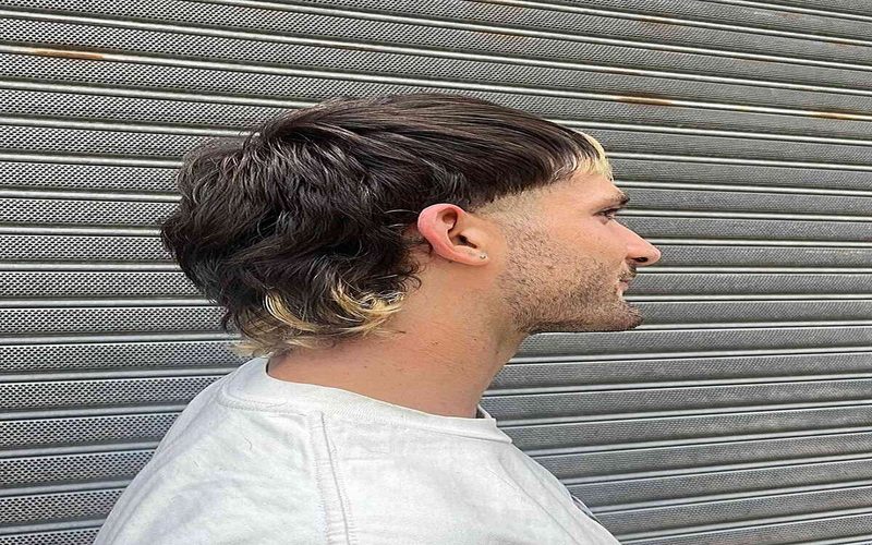 Man with a dyed ends mullet haircut showing wavy medium-length hair, high skin fade, textured top.