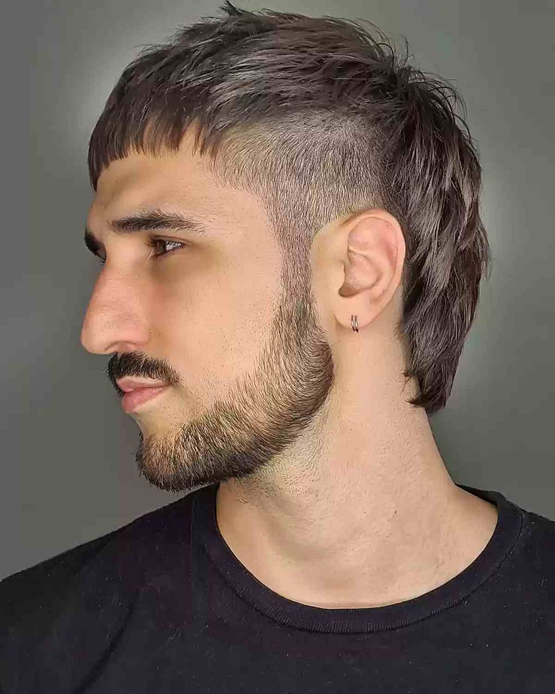 Man with a razor mullet haircut showing textured medium-length hair, low fade, and layered top.