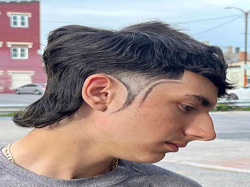 Man with a temp fade mullet haircut showing wavy textured mullet, high skin fade, and sharp line design.