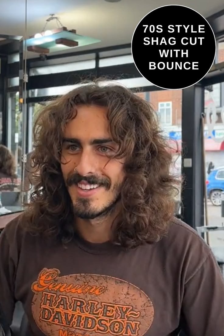 Man with 70s style shag cut, brown curly hair, wearing Harley Davidson shirt, in salon setting.