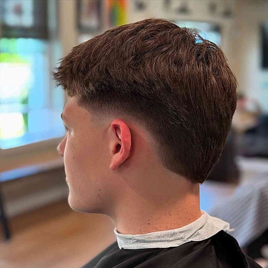 Subtle tapered wolf cut with brown hair, short sides, and textured top, shown from side in a salon setting.