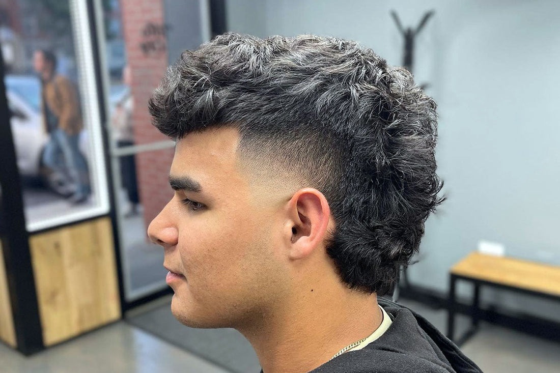 Textured, voluminous top with tight curls; sharp fade on sides.